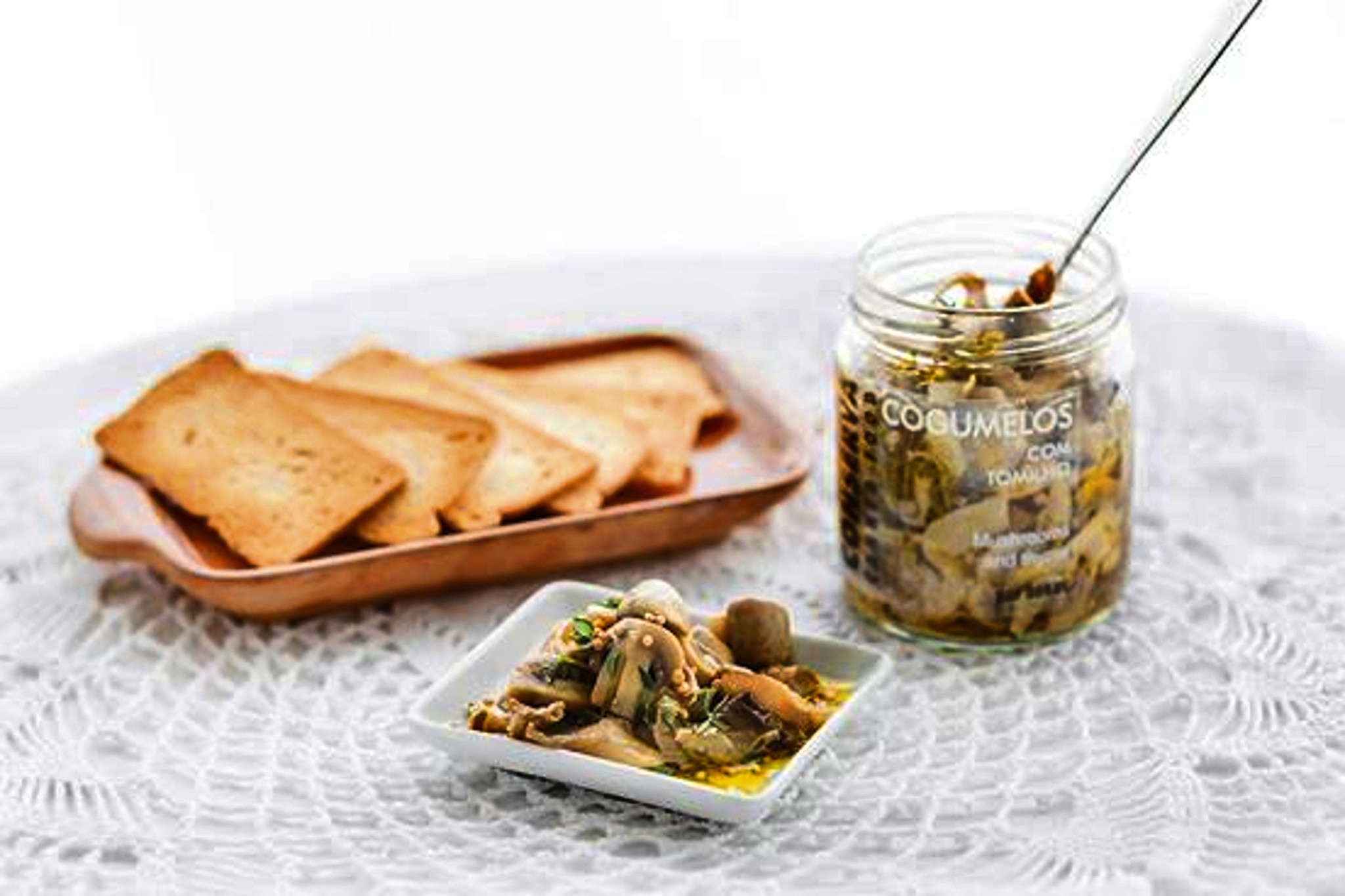 Confitado de cogumelos, malagueta e tomilho, em conserva, servido à mesa com tostas em toalha branca