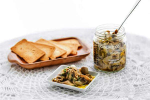 Confitado de cogumelos, malagueta e tomilho, em conserva, servido à mesa com tostas em toalha branca